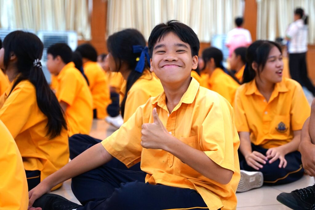 a high school student smiles and gives a thumbs up to the camera