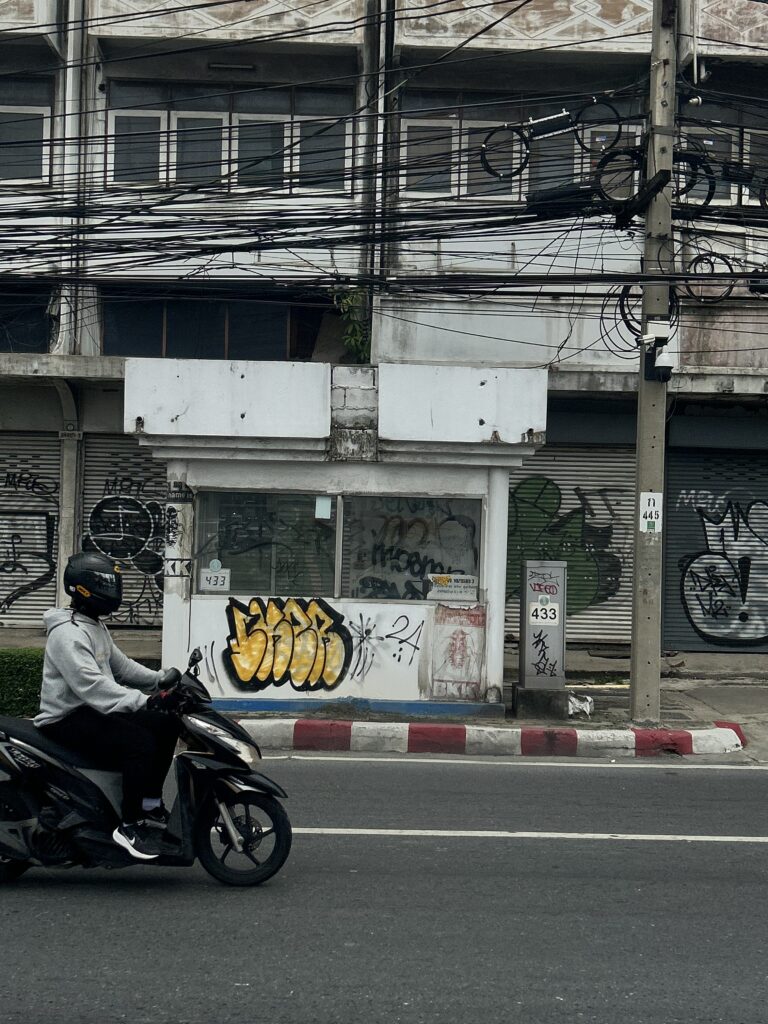 a bike drives along the road in Bangkok behind is a graffitied police booth