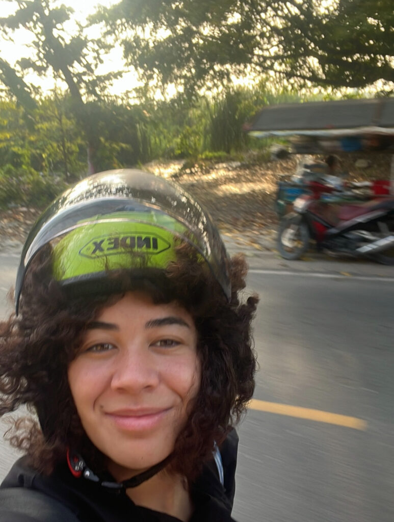 Teacher Athena takes a selfie wearing a helmet while on the back of a bike in Thailand