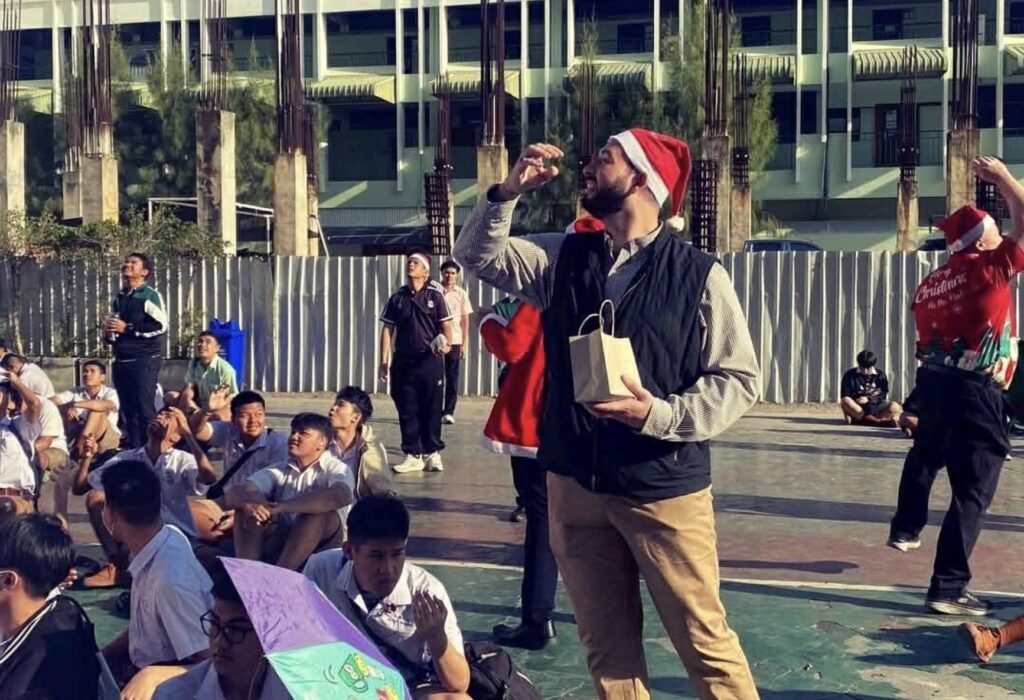 teacher wearing a santa hat plays a game during school celebrations